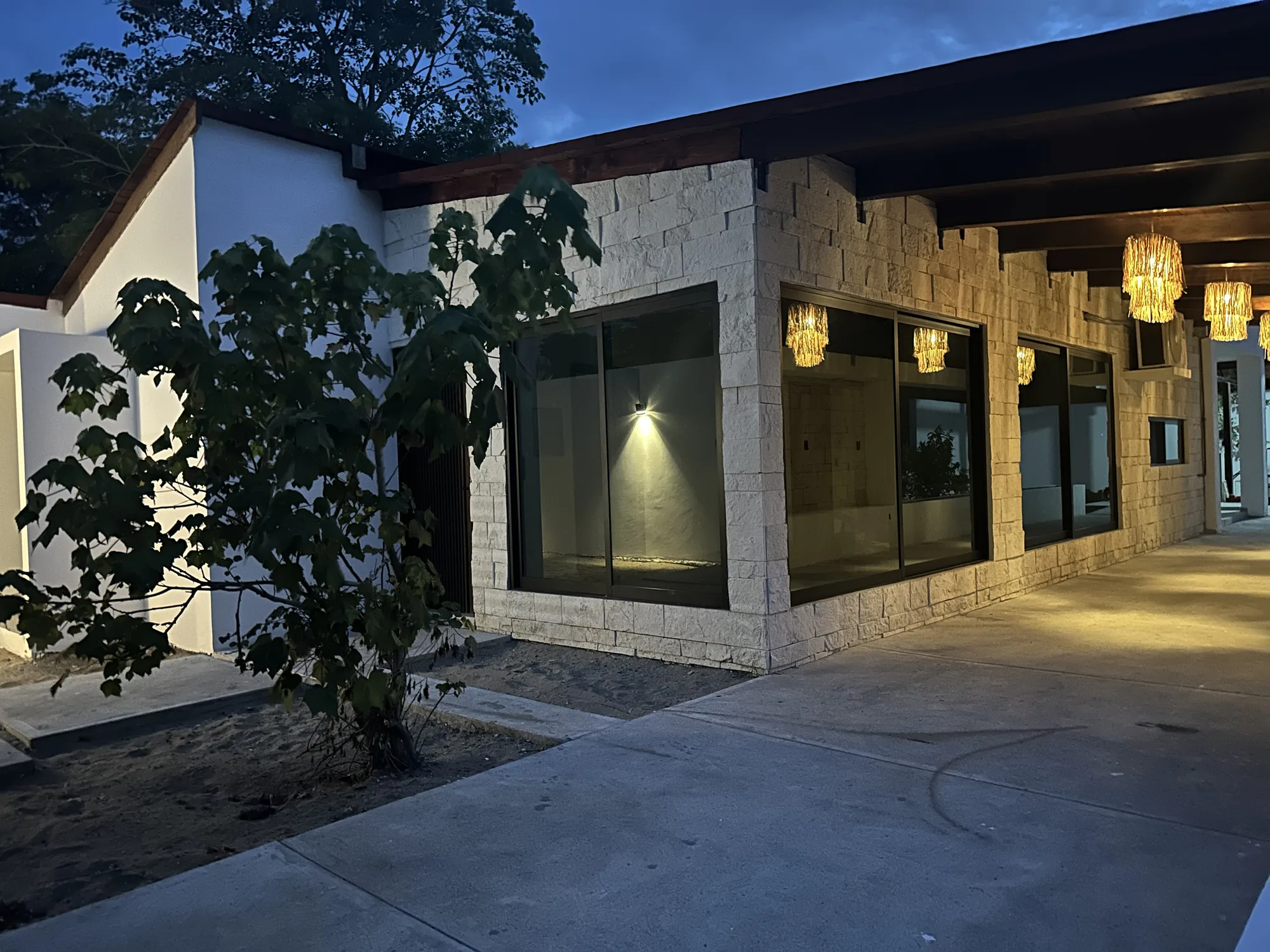 Fachada de proyecto Casa Bastián al atardecer con muros de piedra y lámparas artesanales